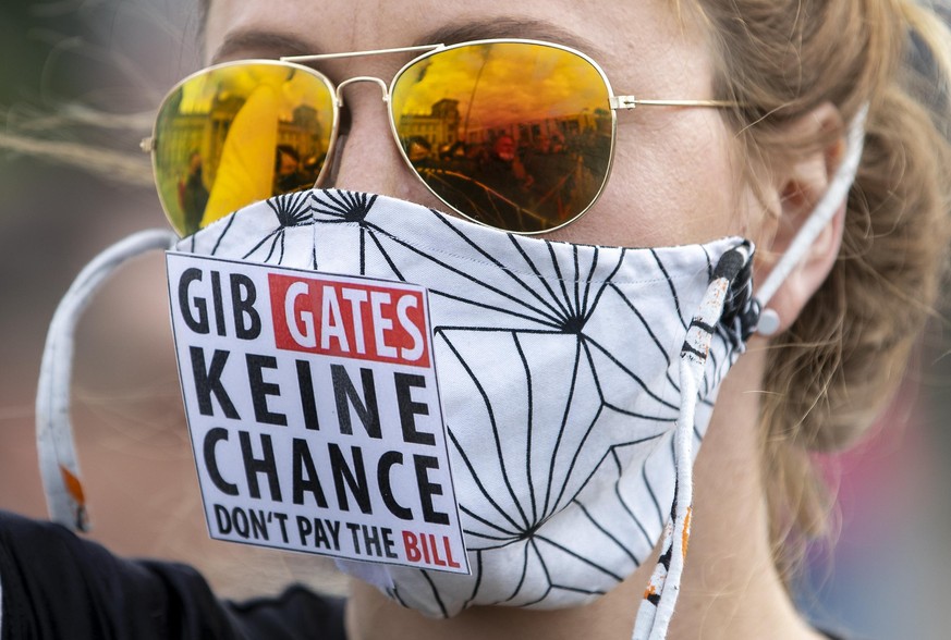 The Reichstag building, home of the German federal parliament, is mirrored in the glasses of a woman wearing a face mask with the slogan &quot;Don&#039;t Give (Bill) Gates A Chance&quot; during a demo ...