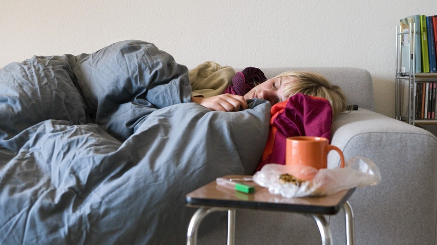 [Themenbild Grippe, gestellte Aufnahme] Eine Frau kuriert auf dem Sofa ihre Grippeerkrankung mit Schlaf aus, aufgenommen am 27. Oktober 2007 in Zuerich. Daneben auf einem Hocker sind eine Tasse Tee, B ...