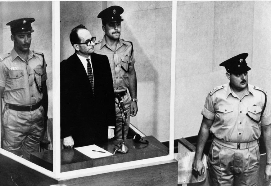 Adolf Eichmann während seines Prozesses im Glaskäfig, flankiert von Polizisten. Er wurde zum Tode verurteilt und in der Nacht vom 31. Mai auf den 1. Juni 1962 durch den Strang hingerichtet.&nbsp;