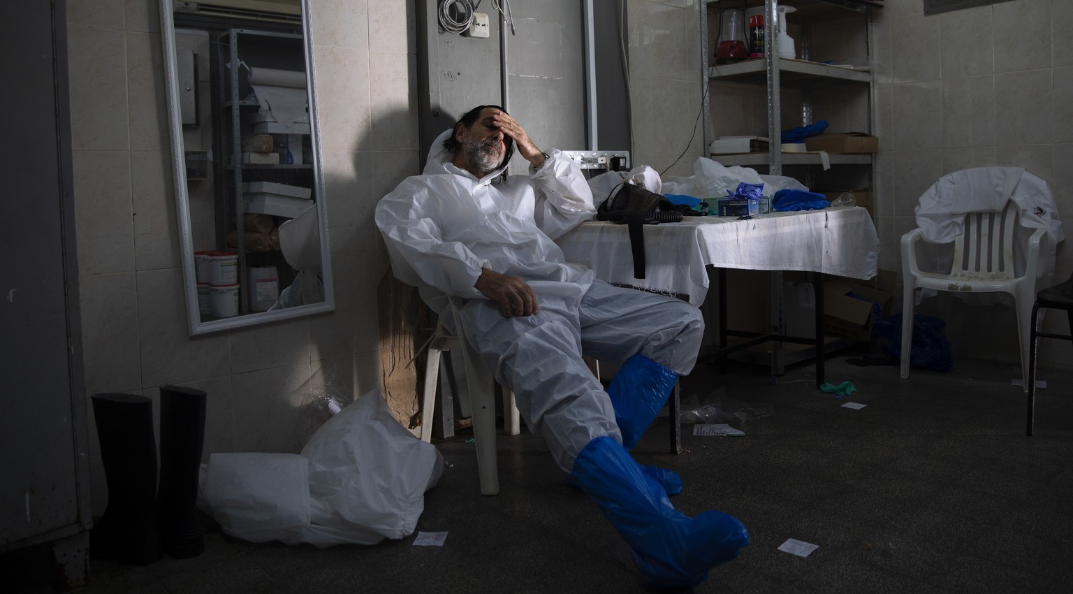 A worker from &quot;Hevra Kadisha,&quot; Israel&#039;s official Jewish burial society, dress in full protective gear rests at a special morgue for people who died from COVID-19, during a nationwide lo ...