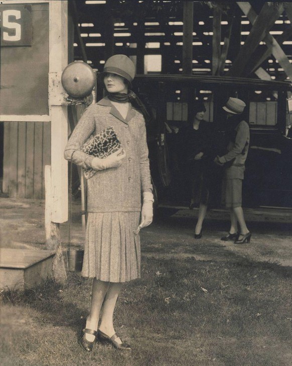 Model wearing a hat and a two-piece tweed dress with box-pleated skirt designed by Drecoll and holding a leopard-print fur envelope purse. (Photo by Edward Steichen/Condé Nast via Getty Images)
