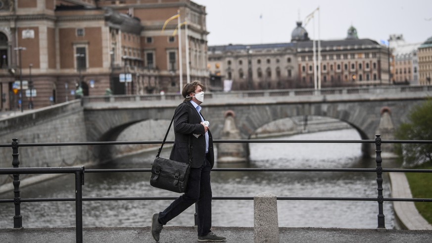 epa08387861 A man wearing a protective mask walks in the rain past the Royal Swedish Opera (at left) in Stockholm, Sweden, 27 April 2020, amid the coronavirus disease (COVID-19) outbreak. EPA/Fredrik  ...