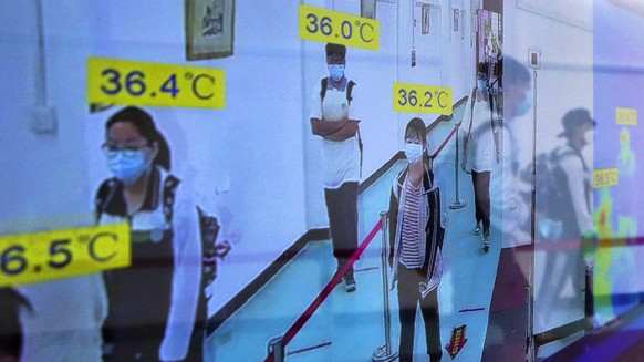 Students wearing protective face masks to help curb the spread of the new coronavirus are reflected on a monitor screen showing their body temperatures as they arrive to a high school in Wuhan in cent ...