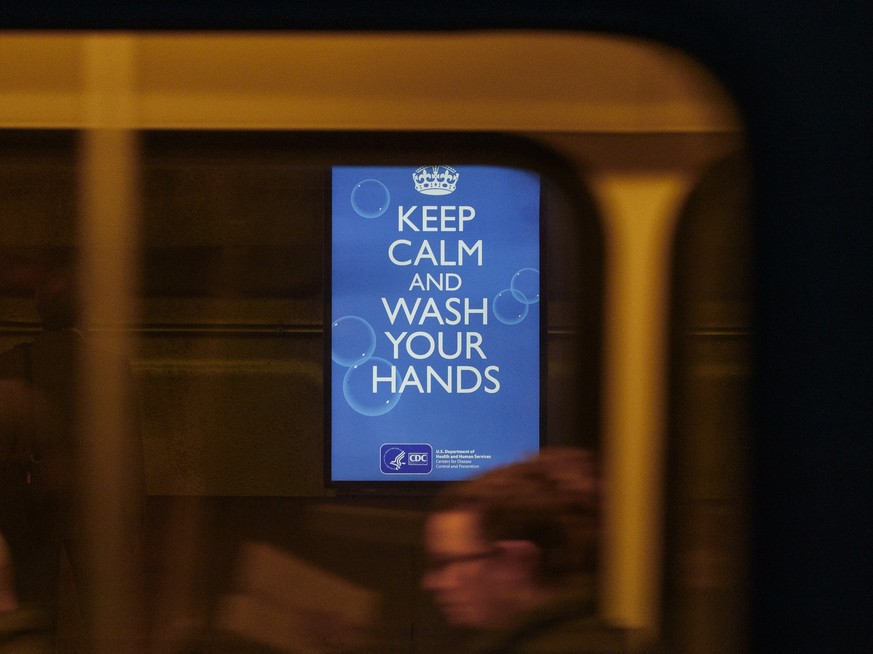 A commuters sit on a train at the Gallery Place Metro subway train platform in Washington, Friday, March 13, 2020, as a video display with a message from the Centers for Disease Control and Prevention ...