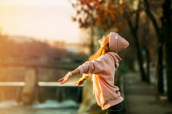 cool hipster young girl in pink hoodie standing by a river in the city very happy smiling to the sun and enjoying it, on autum or springtime