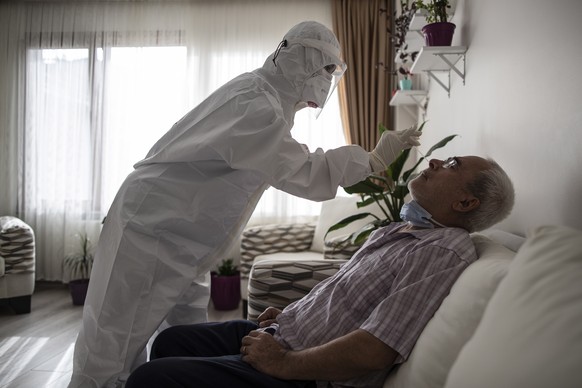 epa08775406 Tugce Atak (L), health worker of Memorial hospital wearing full protective suits takes a swab sample from a man during a Covid-19 test service at home in Istanbul, Turkey, 24 October 2020  ...