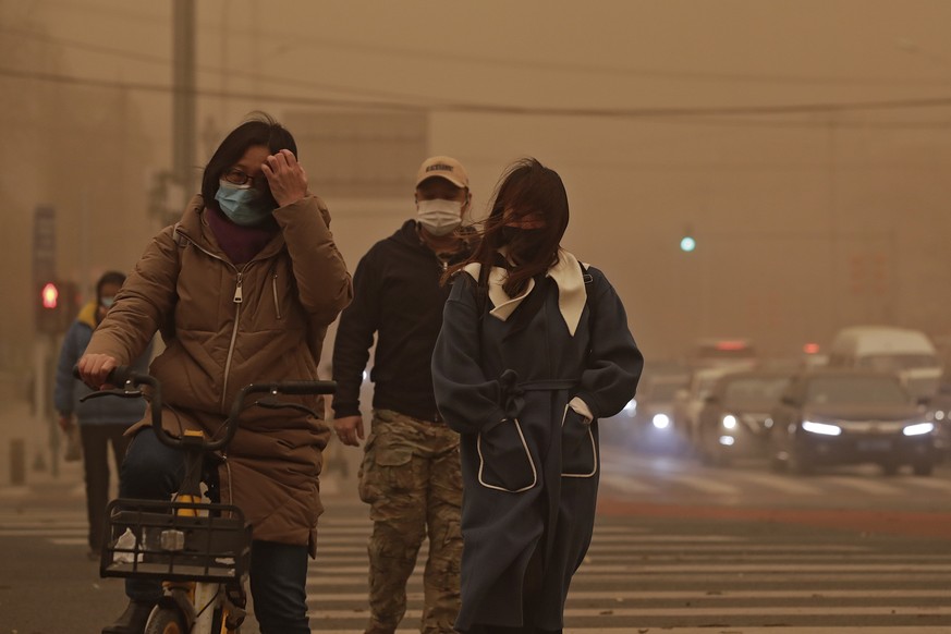 People wearing face masks walk across a street as capital city is hit by polluted air and sandstorm in Beijing, Monday, March 15, 2021. The sandstorm brought a tinted haze to Beijing&#039;s skies and  ...