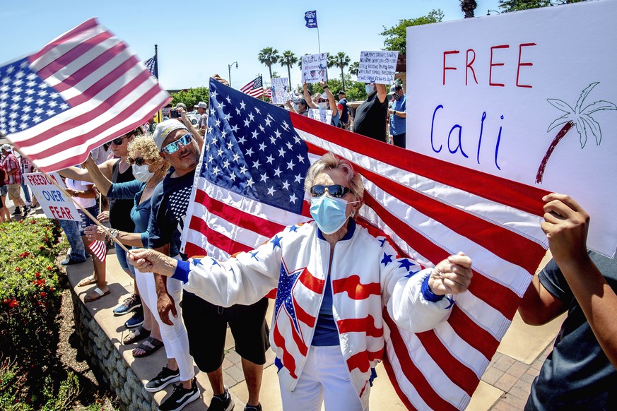Jan Clever, 81, center, of Rancho Cucamonga, center, waves a U.S. flag while wearing a protective mask during a demonstration against California&#039;s stay-at-home orders that were put in place due t ...
