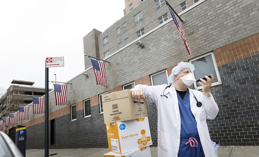 epa08333161 A doctor asks a colleague for help to bring boxes of gloves and masks, donated by the areas Chinese community, inside Elmhurst Hospital Center in Queens, New York, USA, 30 March 2020. New  ...