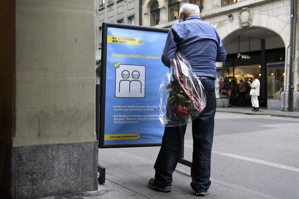Ein Person mit einem Blumenstrauss steht vor einem Plakat mit den Verhaltensregeln des Bundesamtes fuer Gesundheit (BAG), waehrend der Corona-Krise, am Freitag, 16. Oktober 2020 in Bern. (KEYSTONE/Ant ...