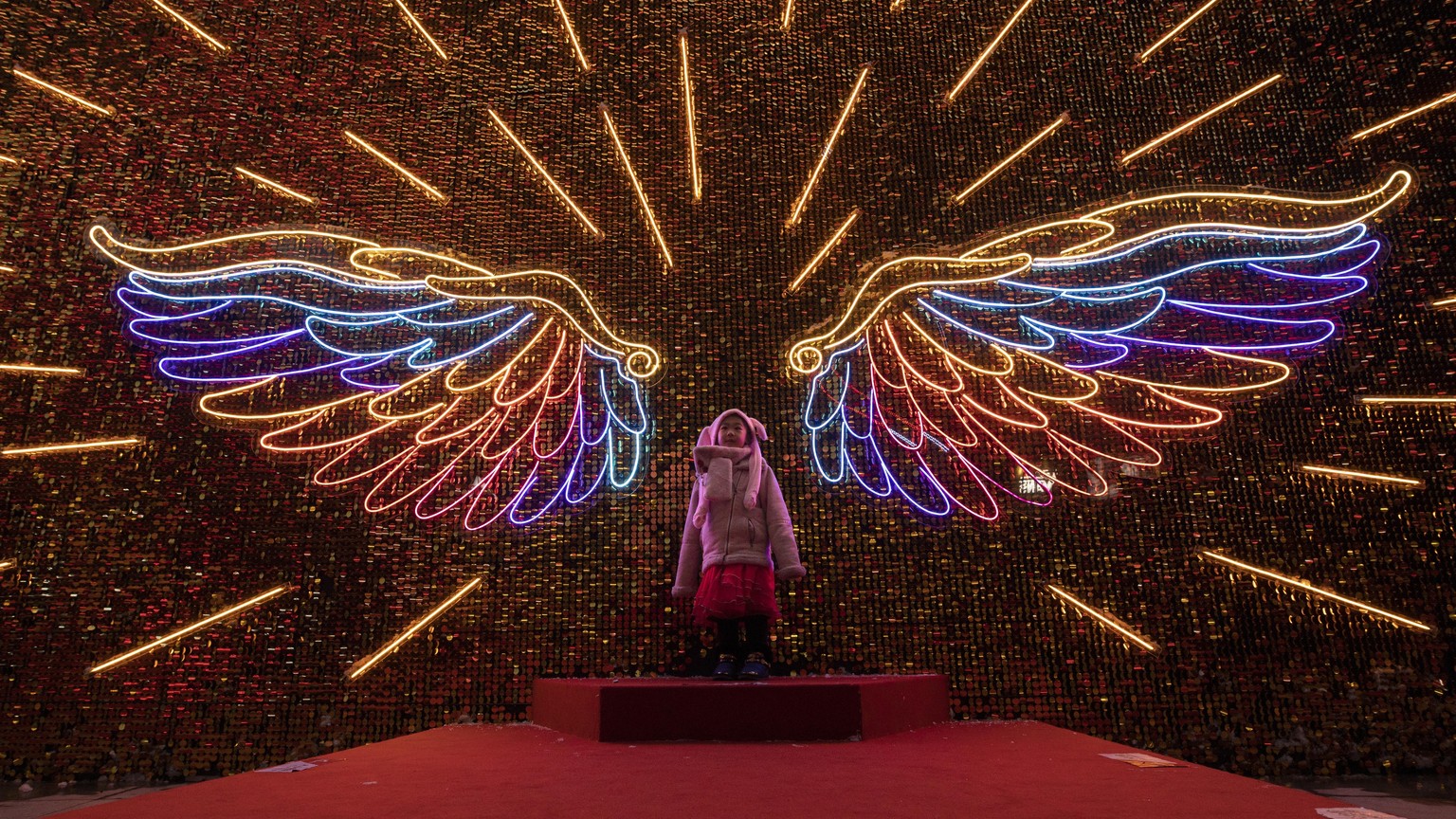 A child poses for photos near wings-shaped neon lights during Christmas Eve in Beijing on Tuesday, Dec. 24, 2019. (AP Photo/Ng Han Guan)