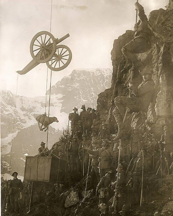 Ca. 1915, Alpen: Italienische Soldaten hieven eine Kiste, einen Hund und ein Artilleriegeschütz auf einen Berg. Hier oben stellte nicht nur der feindliche Beschuss eine Gefahr dar: An manchen Frontabs ...