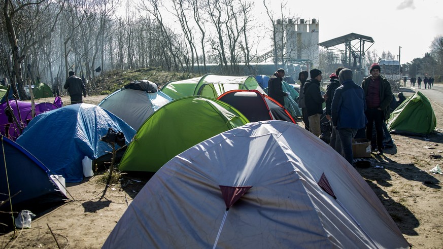 epa08335033 Migrants stand in their camp site in Calais, France, 31 March 2020. The situation of the migrants in Calais is becoming more and more dramatic. Following the confinement measures to halt t ...