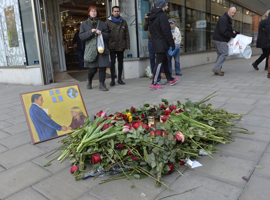 People pass a pile of flowers and a picture at the site where Social Democratic politician, statesman and prime minister Olof Palme was assassinated, on the 30th anniversary of his assassination, at S ...
