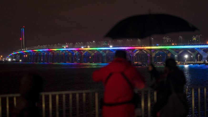 A man takes photographs of the Samuel Champlain Bridge lit up in the colors of the rainbow in solidarity to healthcare workers in Montreal on Sunday, March 29, 2020. (Paul Chiasson/The Canadian Press  ...