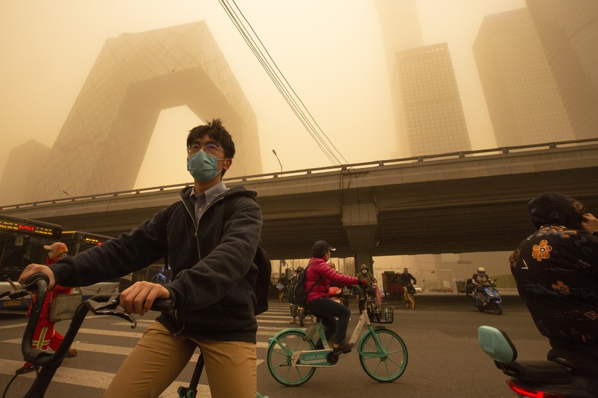 People ride bicycles across an intersection amid a sandstorm during the morning rush hour in the central business district in Beijing, Monday, March 15, 2021. The sandstorm brought a tinted haze to Be ...