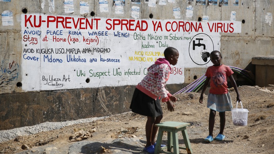 Two young girls sell groundnuts in front of an informational mural advising on precautions to avoid catching the new coronavirus, in the Kibera slum, or informal settlement, of Nairobi, Kenya Thursday ...