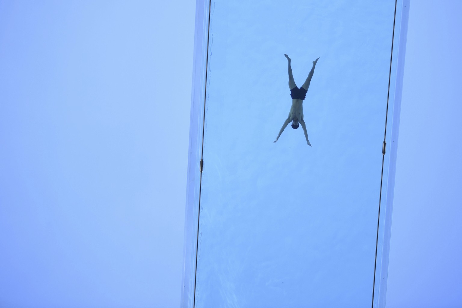 A man swims across the Sky Pool, a transparent swimming pool bridge that spans between two exclusive residential blocks in the Nine Elms area of London, Friday April 23, 2021. The first of its kind, t ...