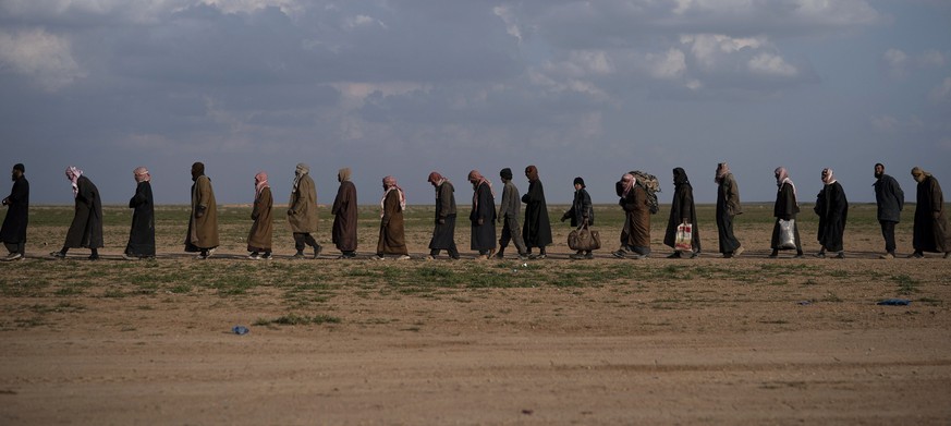 FILE - In this Feb. 22, 2019 file photo, men walk to be screened after being evacuated out of the last territory held by Islamic State militants, near Baghouz, eastern Syria. As Syria marks the eighth ...