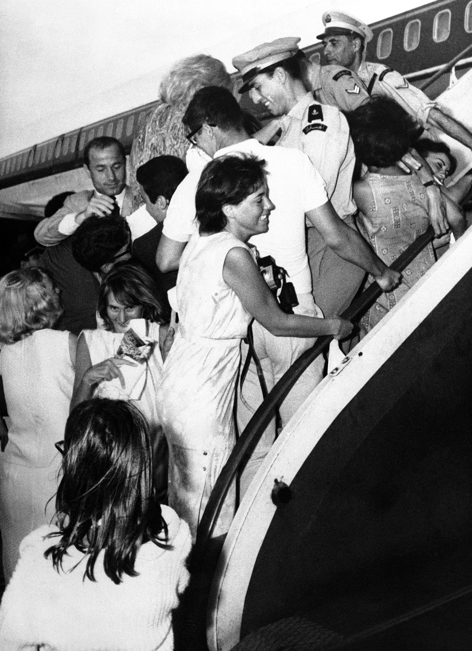 Three overworked policemen straddle the airplane steps to prevent frenzied Lebanese teenagers from clambering aboard the Beatles jet airliner during the pop quartets brief touchdown at Beirut Airport ...