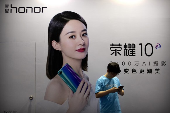 A staff member uses his smartphone in front of a billboard for Chinese smartphone brand Honor at the Global Mobile Internet Conference in Beijing on April 26, 2018. In an announcement Tuesday, Nov. 17 ...