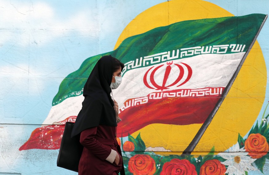 epa08757445 Iranian woman wearing a face mask walks next to Iranian national flag wall painting in Tehran, Iran, 19 October 2020. According to the Iranian Health ministry, Iran reported its highest da ...