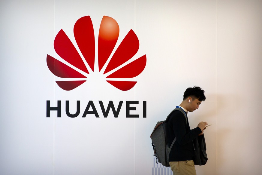 FILE - In this Oct. 31, 2019, file photo, a man uses his smartphone as he stands near a billboard for Chinese technology firm Huawei at the PT Expo in Beijing. Trump administration officials, increasi ...
