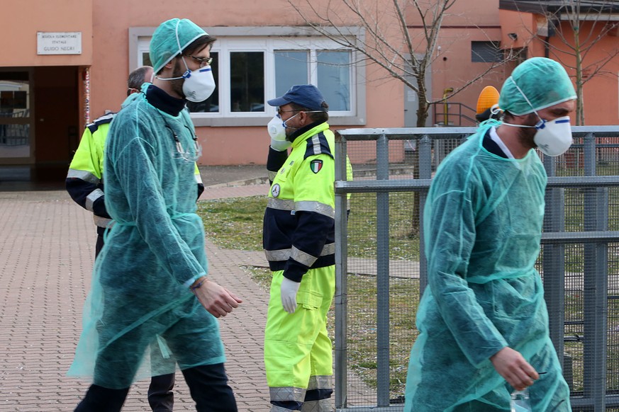 epa08241837 People wear protective face masks in front of a closed elementary school in Vo&#039; Euganeo, Padova, Italy, 23 February 2020. Two deaths from the novel coronavirus sparked fears throughou ...