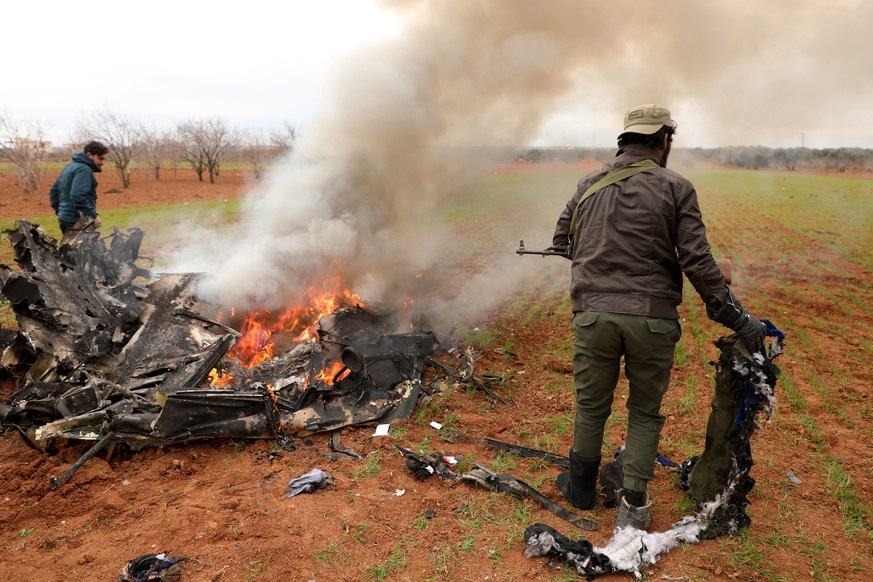 epaselect epa08210776 Armed men stand next to the burning remains of an alleged Syrian army helicopter that was shot down in the village of Qaminas, some four kms east of Idlib, Northern Syria, 11 Feb ...
