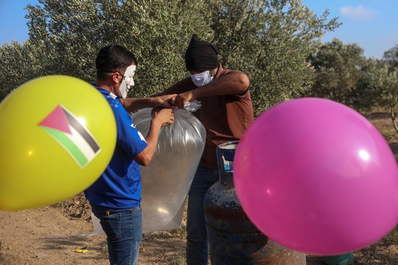 epa08600002 Palestinians wearing masks attach an incendiary device to balloons before realeasing them to Israeli lands near the border between Israel and Eastern Gaza Strip, Gaza Strip, 12 August 2020 ...