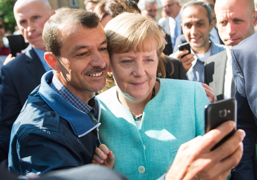 epa04923489 German Chancellor Angela Merkel (R) has a selfie taken with a refugee during a visit to a refugee reception centre in Berlin, Germany, 10 September 2015. Germany can deal with the arrival  ...