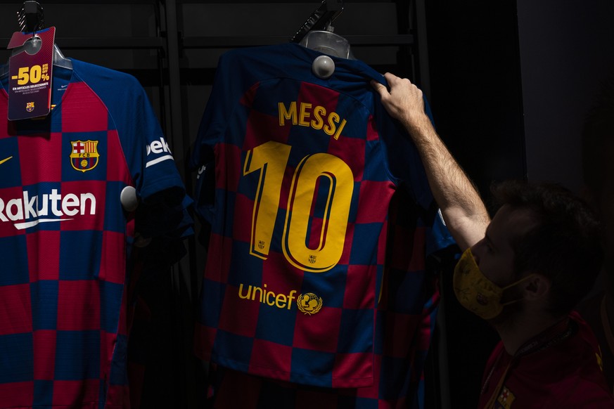 A worker holds a shirt with the name of Barcelona soccer player Lionel Messi at a F.C Barcelona store in Barcelona, Spain on Tuesday, Sept. 1, 2020. Barcelona is banking on a face-to-face meeting with ...