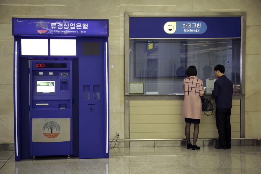 In this April 11, 2017 photo, a man and woman stand at a counter next to a Ryugyong Commercial Bank automated teller machine at the Sunan International Airport in Pyongyang, North Korea. No modern air ...