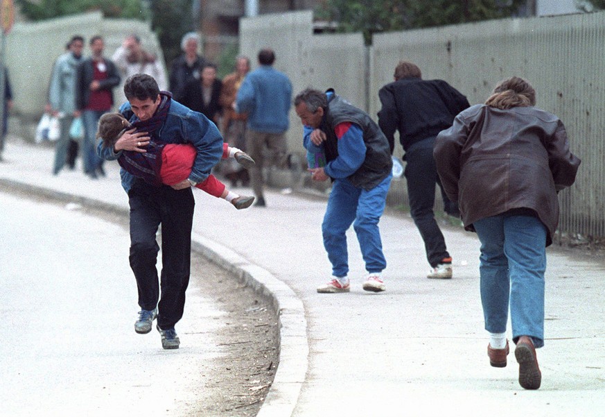 An April 1993 photo shows a Bosnian man cradling his child as they and others run past one of the worst spots for sniper attacks in Sarajevo. (AP Photo/Michael Stravato)