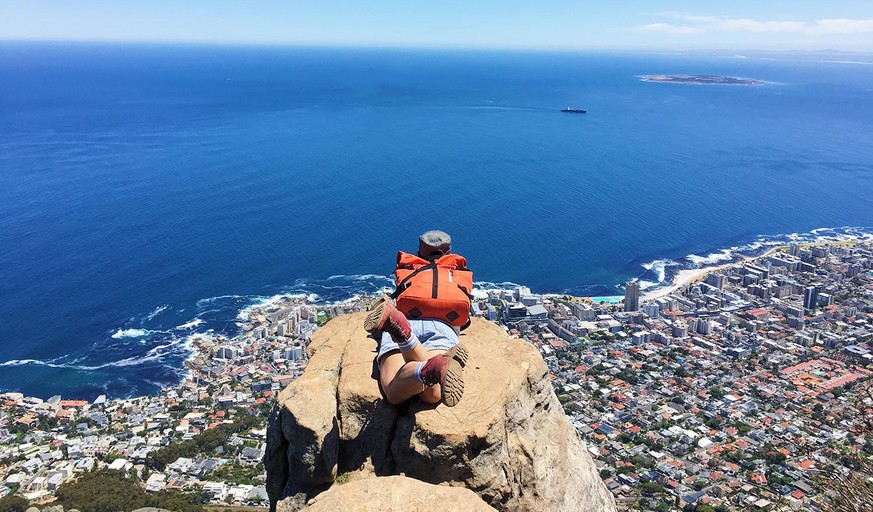 A girl sleep on a rock on top of Lion&#039;s head mountain overlooking the city and dark blue sea below with blue sky in Cape Town South Afica.