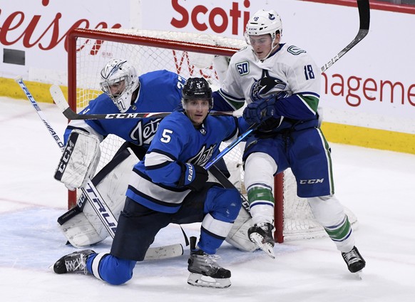Winnipeg Jets&#039; Luca Sbisa (5) and Vancouver Canucks&#039; Jake Virtanen (18) battle for position in front of Jets goaltender Connor Hellebuyck (37) during the third period of an NHL hockey game T ...