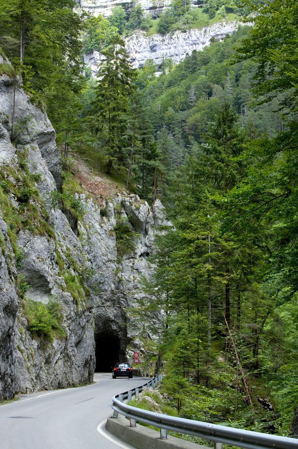 On the road that follows the creek &quot;La Sorne&quot;, a car is about to disappear in a tunnel underneath the &quot;Les Rochers Bacon&quot; cliffs near Undervelier in the canton of Jura, Switzerland ...