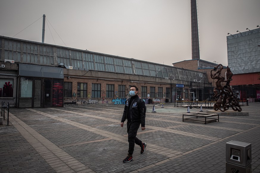 epa08274632 A man wearing a medical face mask walks on an empty street next to the 798 Art District in Beijing, China, 06 March 2020. Daily life in Beijing has been heavily affected by the outbreak of ...