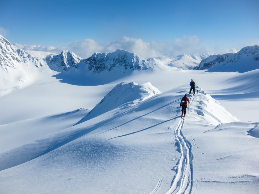 Höhenblick auf zwei Skifahrer, die auf einem Bergkamm in den Lyngenalpen, Norwegen, wandern.