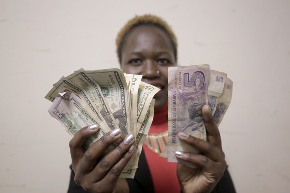 epa07670918 A woman holds the Zimbabwe dollar notes and the US dollars in Harare, Zimbabwe 24 June 2019. the government of Zimbabwe has banned the sale of goods in a foreign currency other than the lo ...
