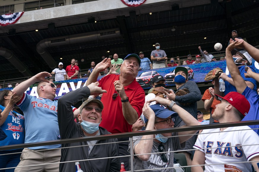 Fans scramble for a foul ball during the first inning of a baseball game between the Texas Rangers and the Toronto Blue Jays, Monday, April 5, 2021, in Arlington, Texas. (AP Photo/Jeffrey McWhorter)