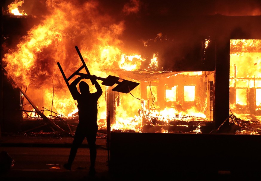 MINNEAPOLIS, MINNESOTA - MAY 29: A man holds up a sign near a burning building during protests sparked by the death of George Floyd while in police custody on May 29, 2020 in Minneapolis, Minnesota. E ...