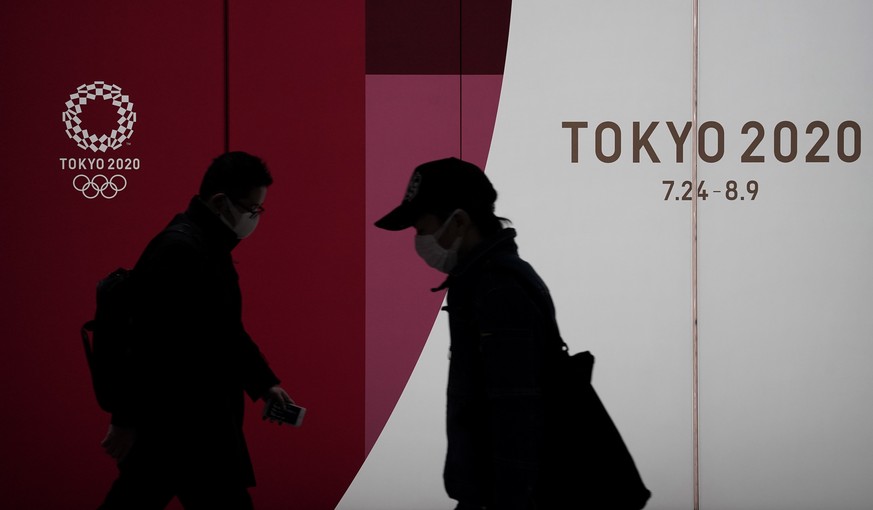 epaselect epa08315000 Pedestrians wearing masks walk past the emblem of the Tokyo Olympic Games in Tokyo, Japan, 23 March 2020. Japanese Prime Minister Shinzo Abe said on 23 March 2020 that postponeme ...
