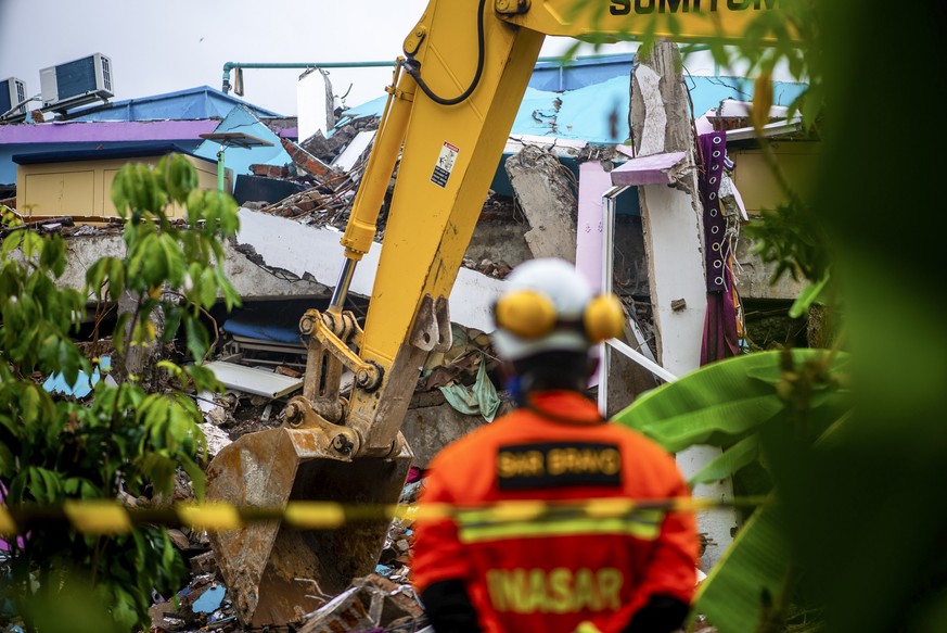 epa08943005 An excavator cleans up the heavy ruin as a member of Indonesian search and rescue (BASARNAS) looks on at a collapsed building hit by the 6.2 magnitude earthquake in Mamuju, West Sulawesi,  ...