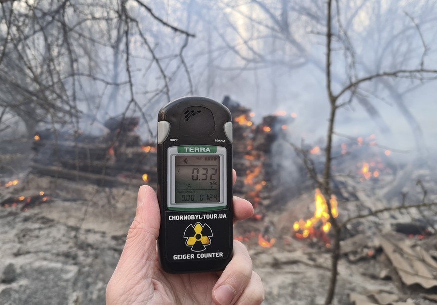 epaselect epa08348334 A man holds a dosimeter close to an abandoned house burning in the middle of a forest fire near the village of Volodymyrivka, in the exclusion zone around the Chernobyl nuclear p ...