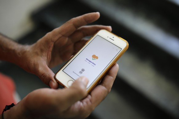 In this Thursday, May 7, 2020 photo, an Indian man uses Aarogya Setu app on his mobile phone in New Delhi, India. As India enters an extended coronavirus lockdown, the government is fervently pursuing ...