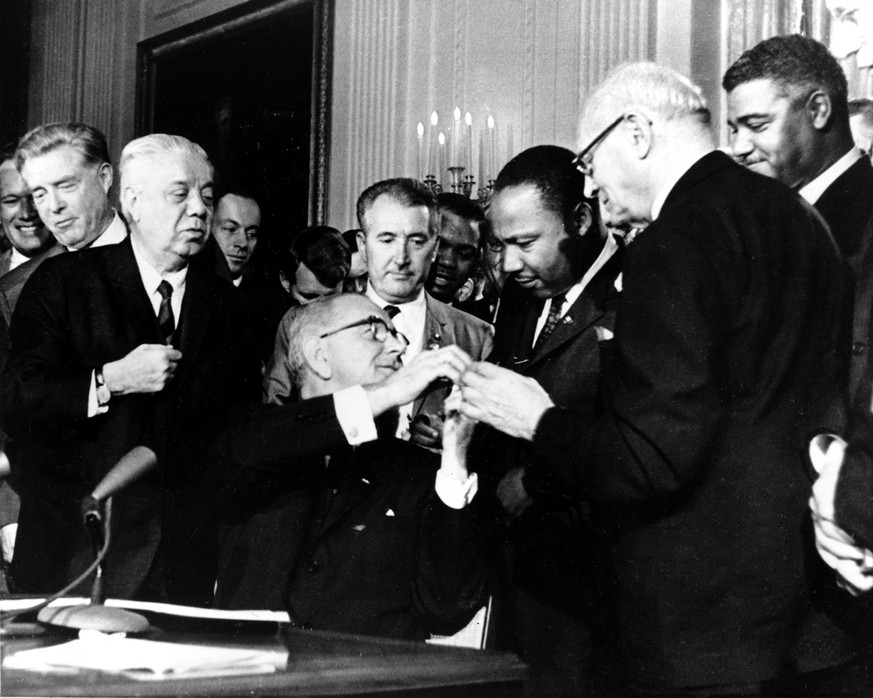 Präsident Johnson (M.) überreicht Martin Luther King den Füllhalter, mit dem er das Bürgerrechtsgesetz unterschrieben hat.&nbsp;