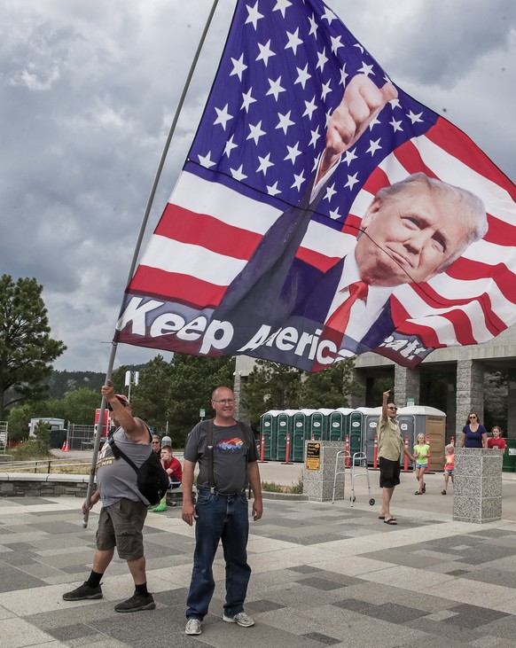 epa08524059 A man poses for a picture as another one files a flag supporting US President Donald J. Trump at the Mt. Rushmore National Monument in Keystone, South Dakota, USA, 02 July 2020. US Preside ...