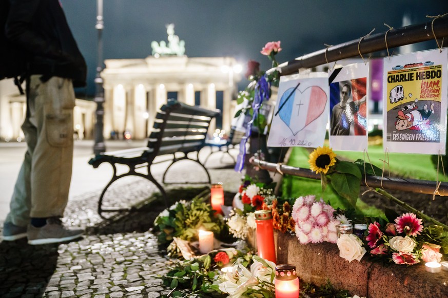 epa08757863 Candles, messages and floral tributes are placed at the site of a vigil to pay respect to beheaded French teacher Samuel Paty in front of the French embassy, near the landmark Brandenburg  ...