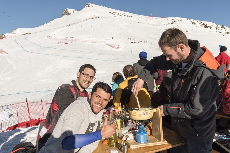 Spectators enjoy a cheese fondue, with the track and the Lauberhorn in the background, as a ski racer approaches the curve above the Hundschopf during the men&#039;s downhill race at the Alpine Skiing ...